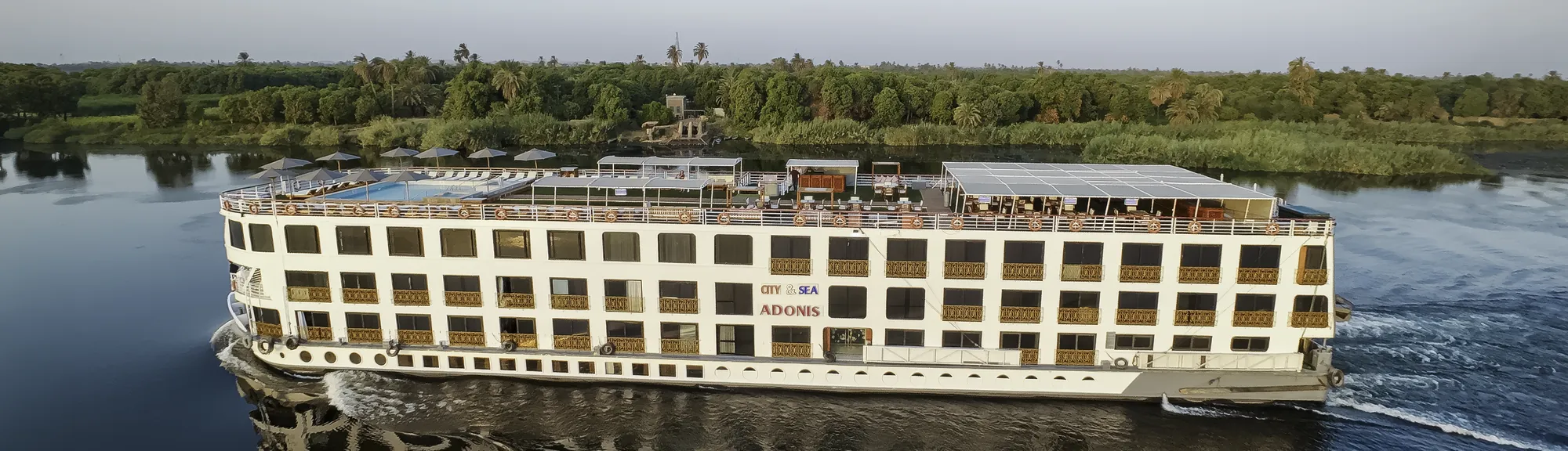 M/S City and Sea Adonis sailing past palm-lined riverbanks