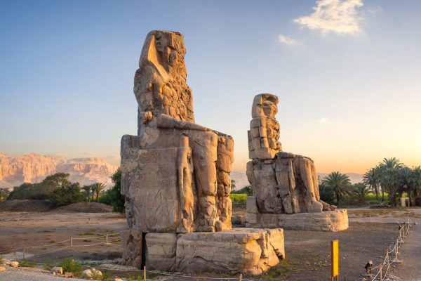 Colossi of Memnon, two massive stone statues at sunset in Luxor, Egypt.
